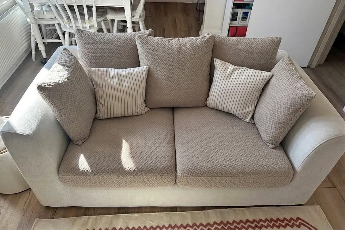 A beige 2-seater sofa with textured covers and striped accent pillows in a bright living room with natural light.