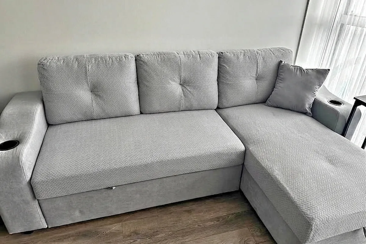 Light grey patterned sofa cover on a modern L-shaped sectional sofa with cup holders in a bright living room.